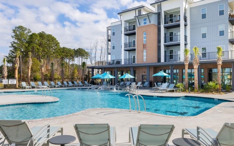 Outdoor swimming pool at Restore at Carolina Park apartments in Mt. Pleasant, SC, featuring lounge chairs and umbrellas.